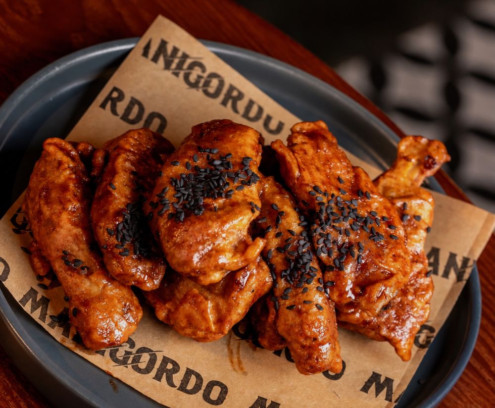 Alitas doradas con salsa y ajonjolí negro sobre papel de Manigordo